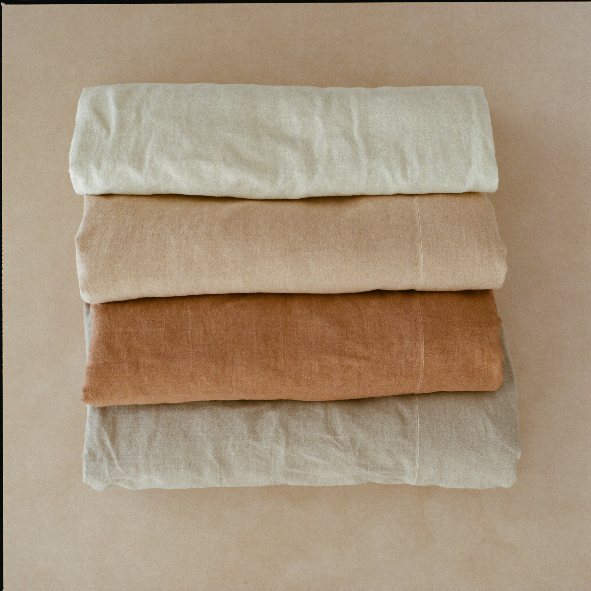 Set fra oven: foldet sengelinned stablet i en tonal gradient fra cremehvid til lertone.
